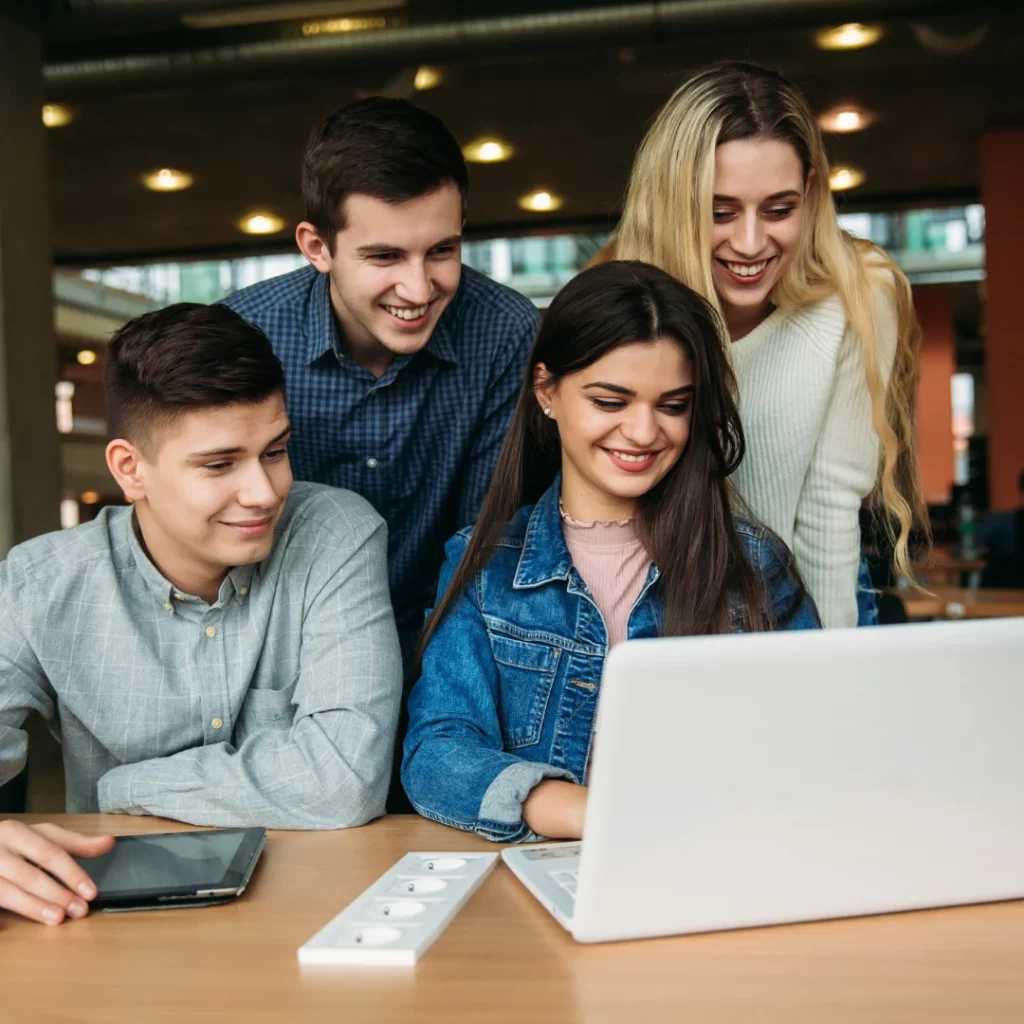 A group of young adults collaborating on a laptop in a modern learning environment, representing teamwork and skill development at GBC Skills.